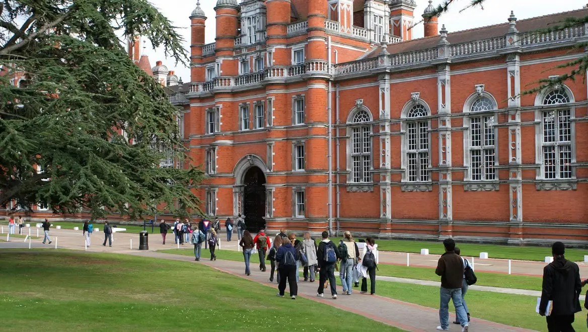Students walking across a university campus outside a historic academic building, representing college life and student experiences