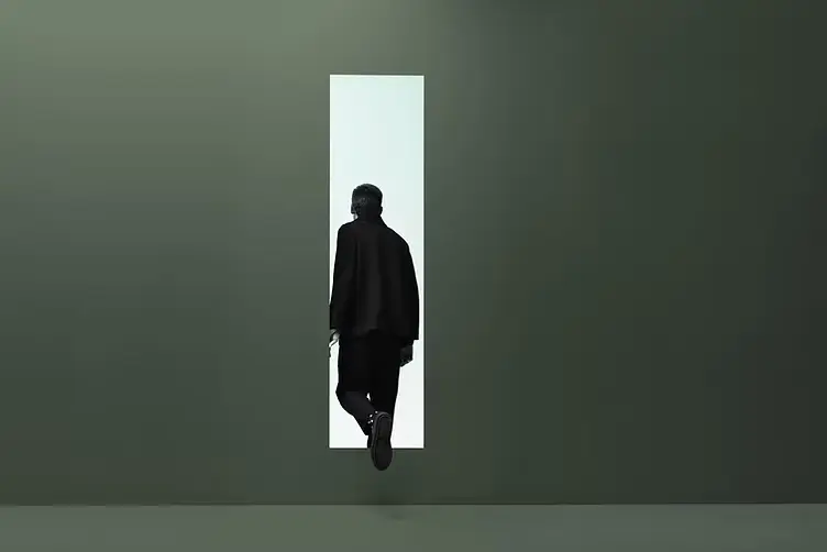Person walking away into a narrow doorway, representing grief, loss, isolation, and the emotional transition after death